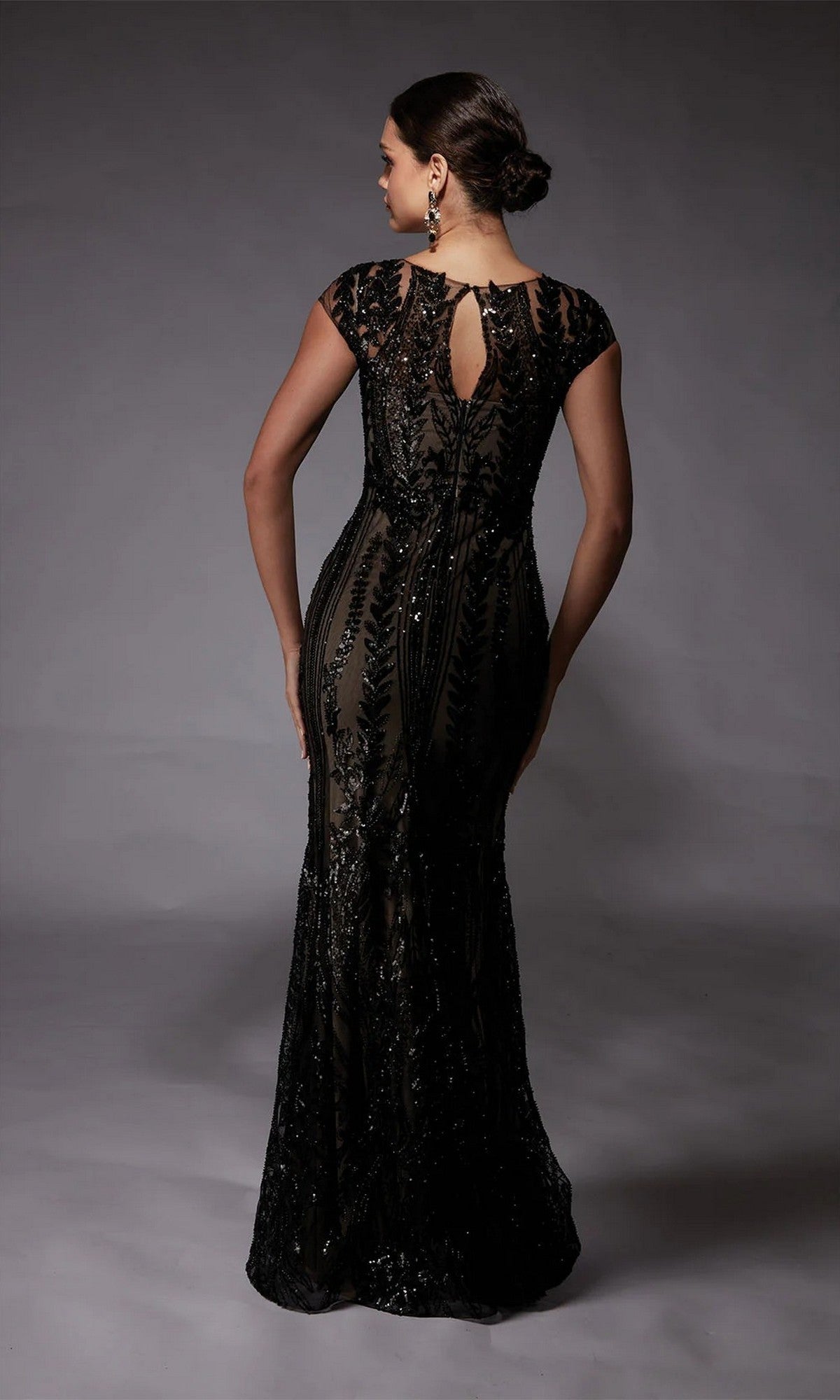 A woman faces away in the Alyce 27716, a floor-length sequin dress with cap sleeves and a keyhole back. Her hair is styled in a low bun—an elegant mother-of-the-bride formal gown.
